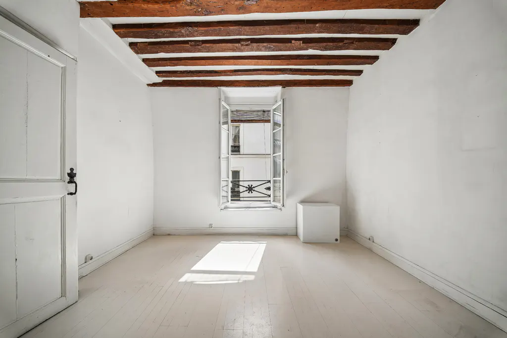 Empty white room with exposed wood beams on ceiling, open window, and white painted wood floors.