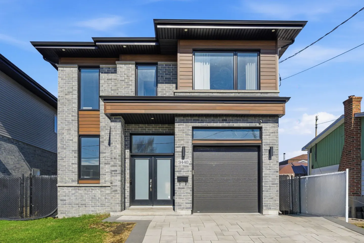 Two-story modern house with gray brick, wood accents, black trim, a garage, and a paved driveway.