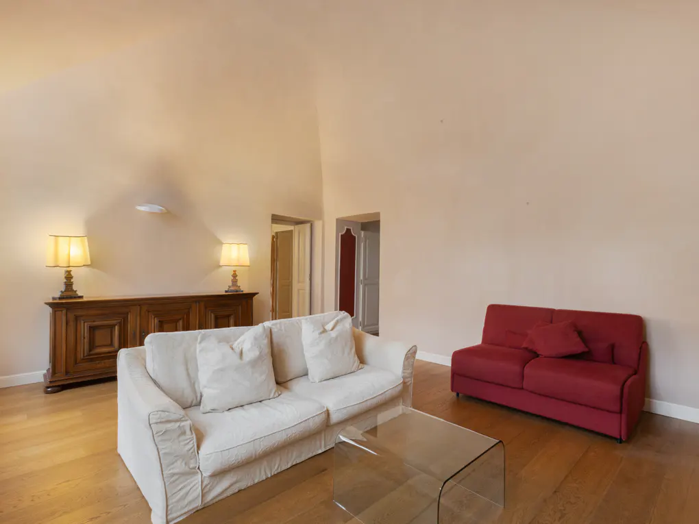 Living room with a white sofa, red loveseat, glass table, and wooden cabinet with lamps on a wood floor.