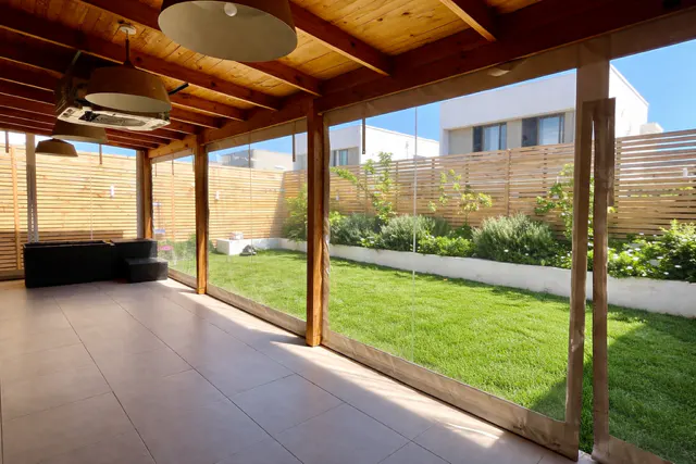 Covered patio with wood ceiling, tile floor, and clear vinyl curtains. A green lawn and wood fence are visible outside.