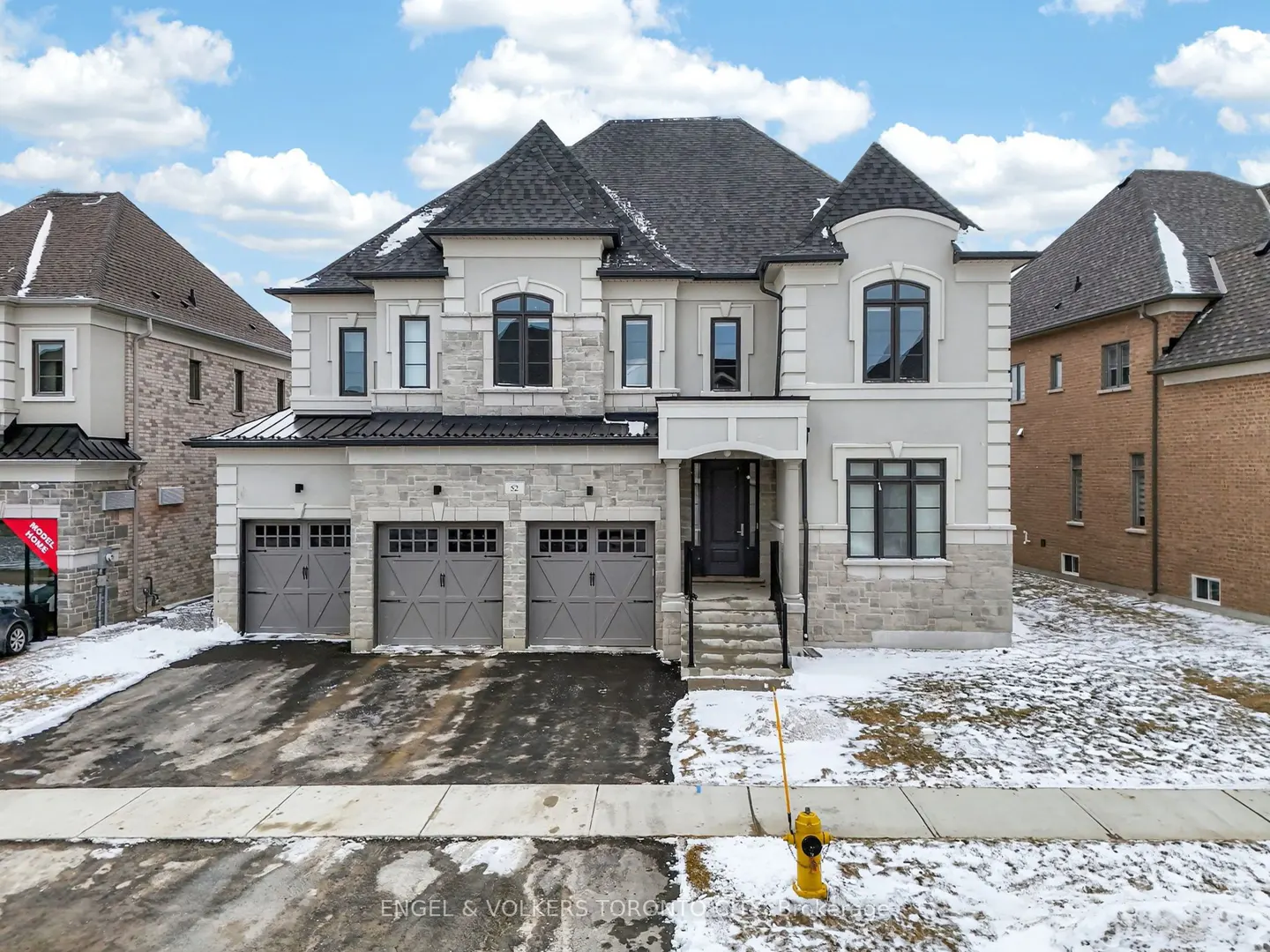 Exterior view of a two-story house with a three-car garage, gray doors, stone accents, and a dark roof.