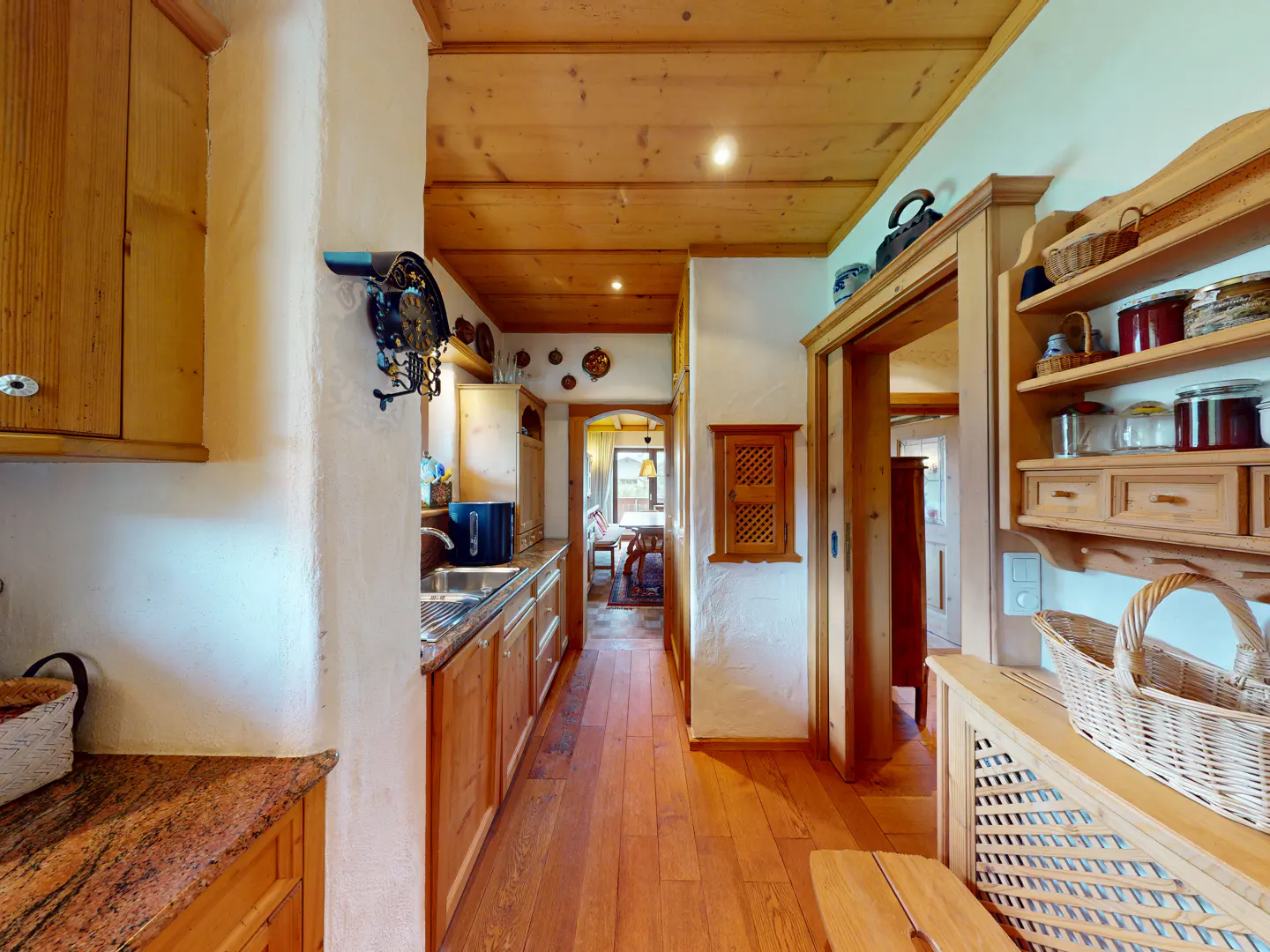 Rustic kitchen with wood paneling, cabinets, and flooring, featuring a wicker basket and open shelving in a cozy home.