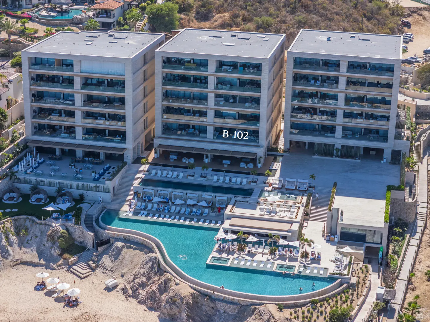 Aerial view of a luxury resort with three modern, multi-story buildings, pools, beach access, and ocean views.