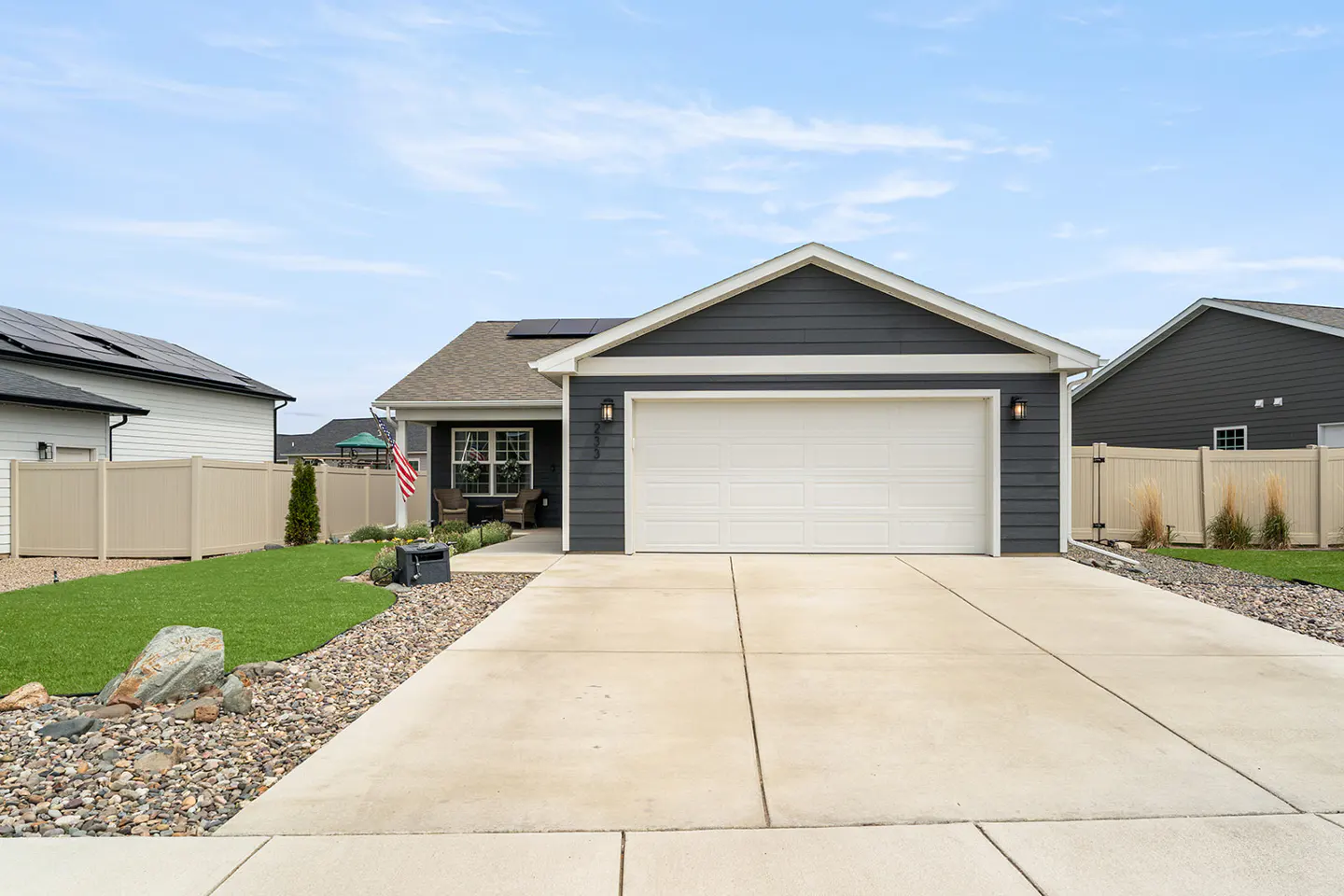Front view of a one-story house with gray siding, a white garage door, and a concrete driveway.