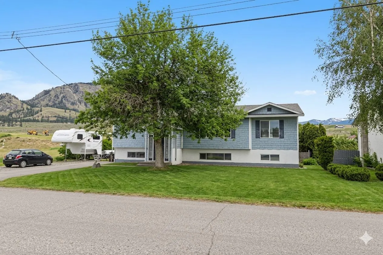 Exterior of a light blue two-story house with a large tree in the front yard. A car and RV are parked in the driveway. Mountains are in the background.