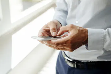 Person using a smartphone while standing by a window