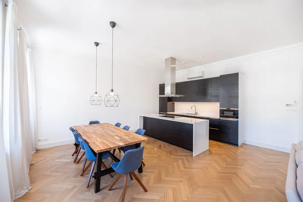 Bright, modern kitchen and dining area with wood floors, black cabinets, island, and a wood table with blue chairs.