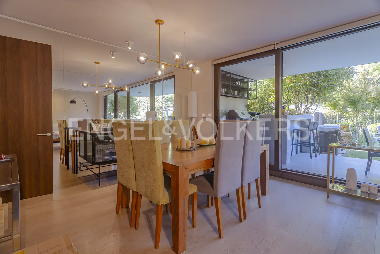 A dining room with a wooden table, chairs, and a modern chandelier. Sliding glass doors lead to an outdoor patio.