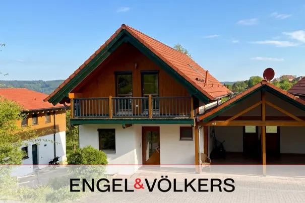 A two-story house with a red roof, brown wood, and white walls, with a balcony and a carport.
