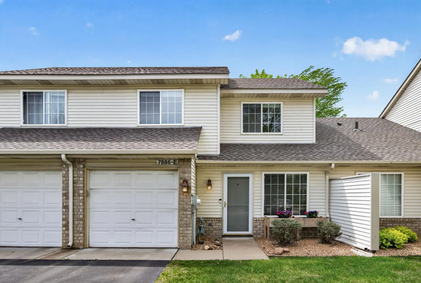 Beige two-story townhouse with white garage door, front door, and windows under a blue sky.