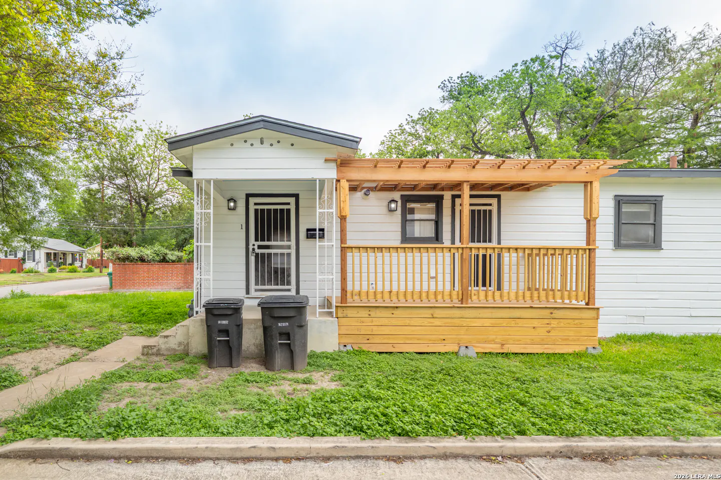 Exterior of a white house with a wooden porch and black trim. Two black trash cans sit in front.