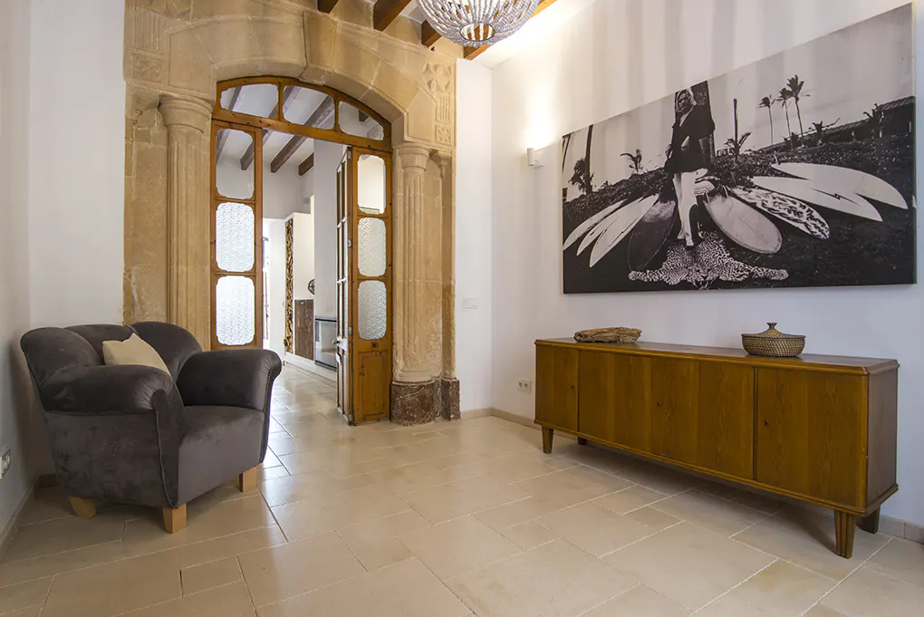 Interior view of a room with a gray armchair, wooden cabinet, and a black and white photo of a surfer with surfboards.
