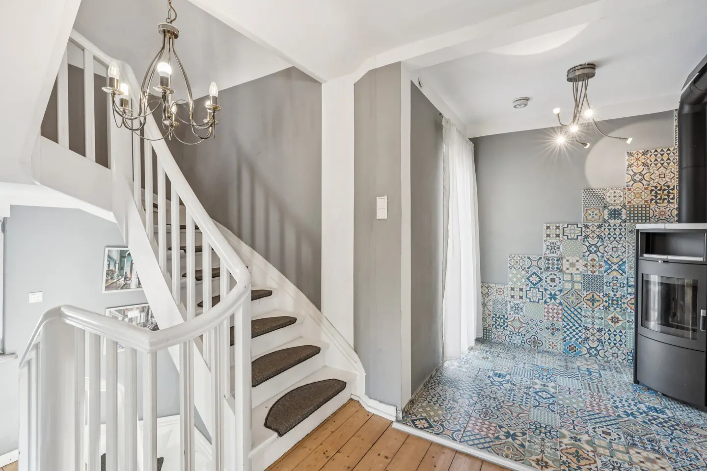 Interior view of a home featuring a white staircase with brown treads, a chandelier, and patterned tile flooring.