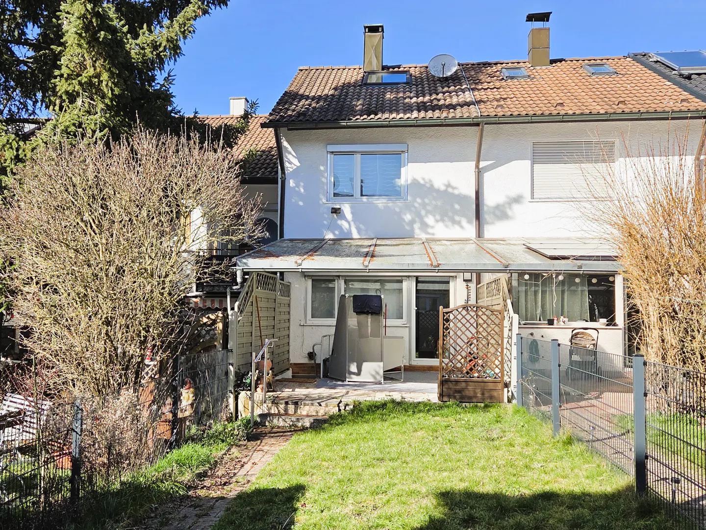 Backyard view of a two-story white townhouse with a red tile roof, a small patio, and a green lawn.