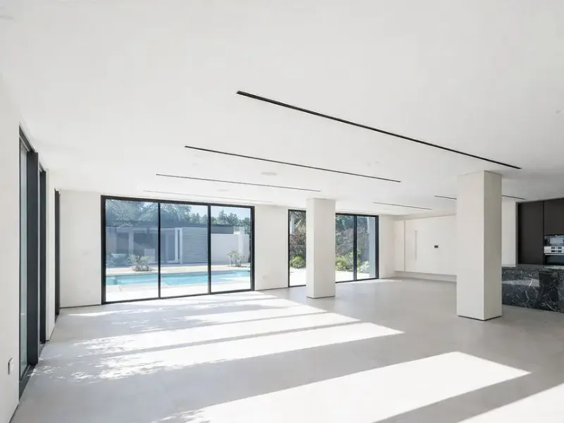 Bright, modern room with white walls, black-framed windows, and a view of a pool. Sunlight streams across the floor.