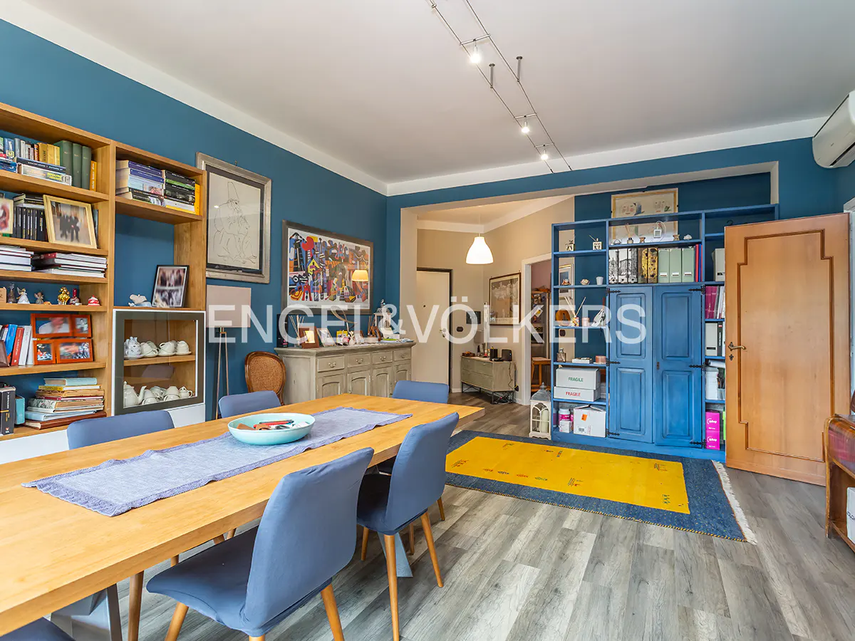 A dining room with blue walls, a wooden table with blue chairs, and a bookshelf filled with books and decorations.