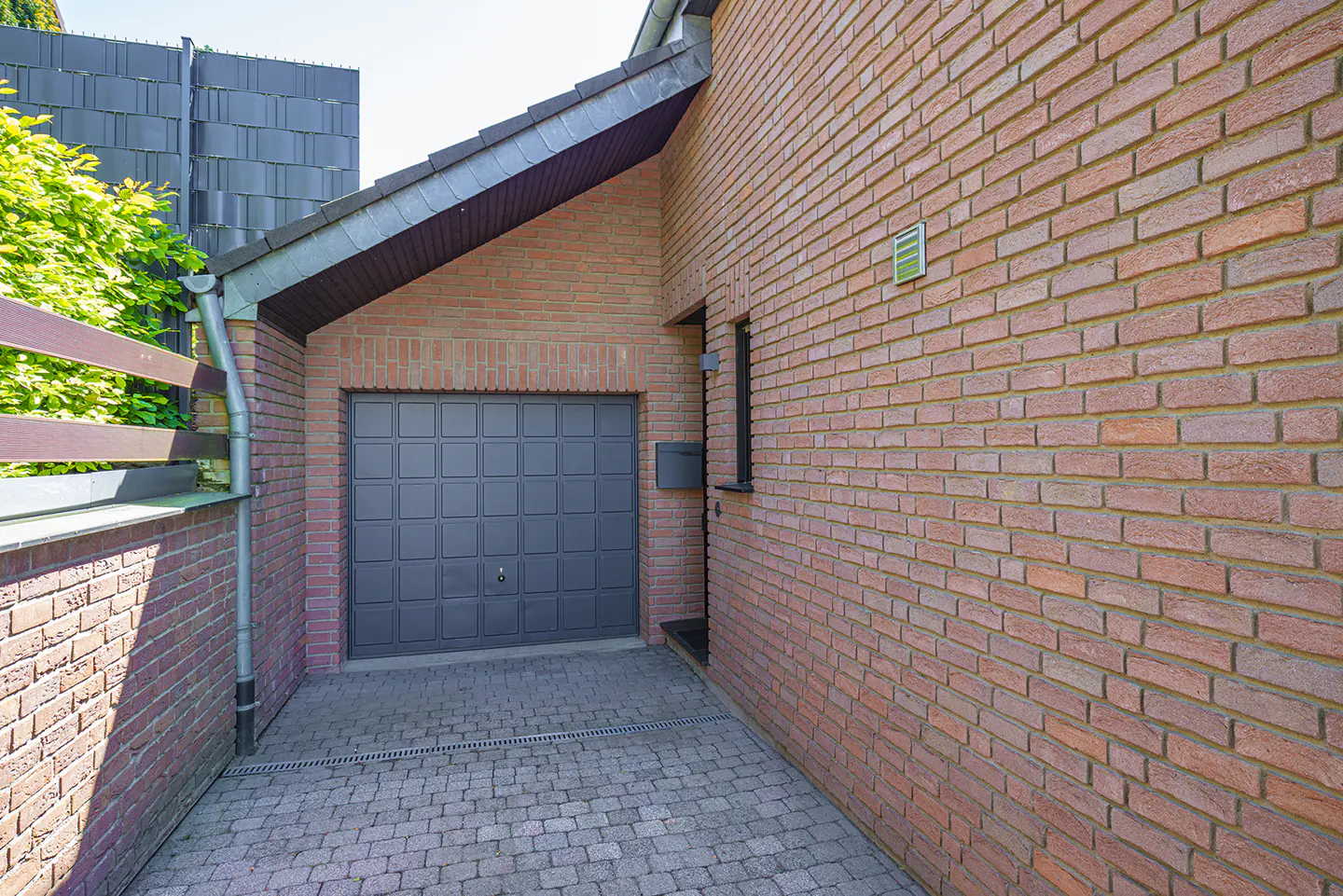 Brick house exterior with a gray garage door and a brick-paved driveway.
