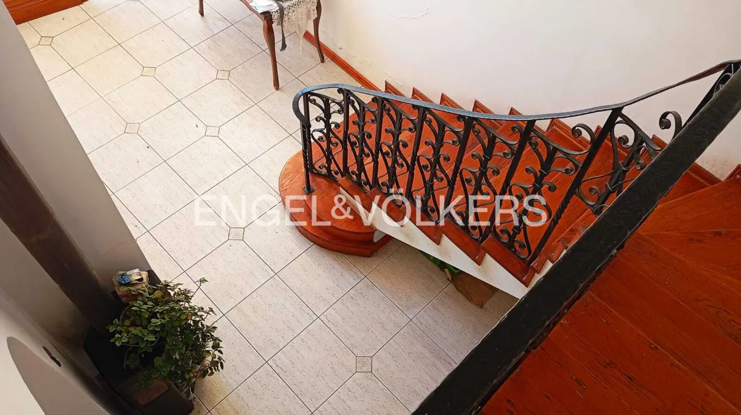 Overhead shot of a foyer with beige tile, a wooden staircase with black iron railing, and a potted plant.