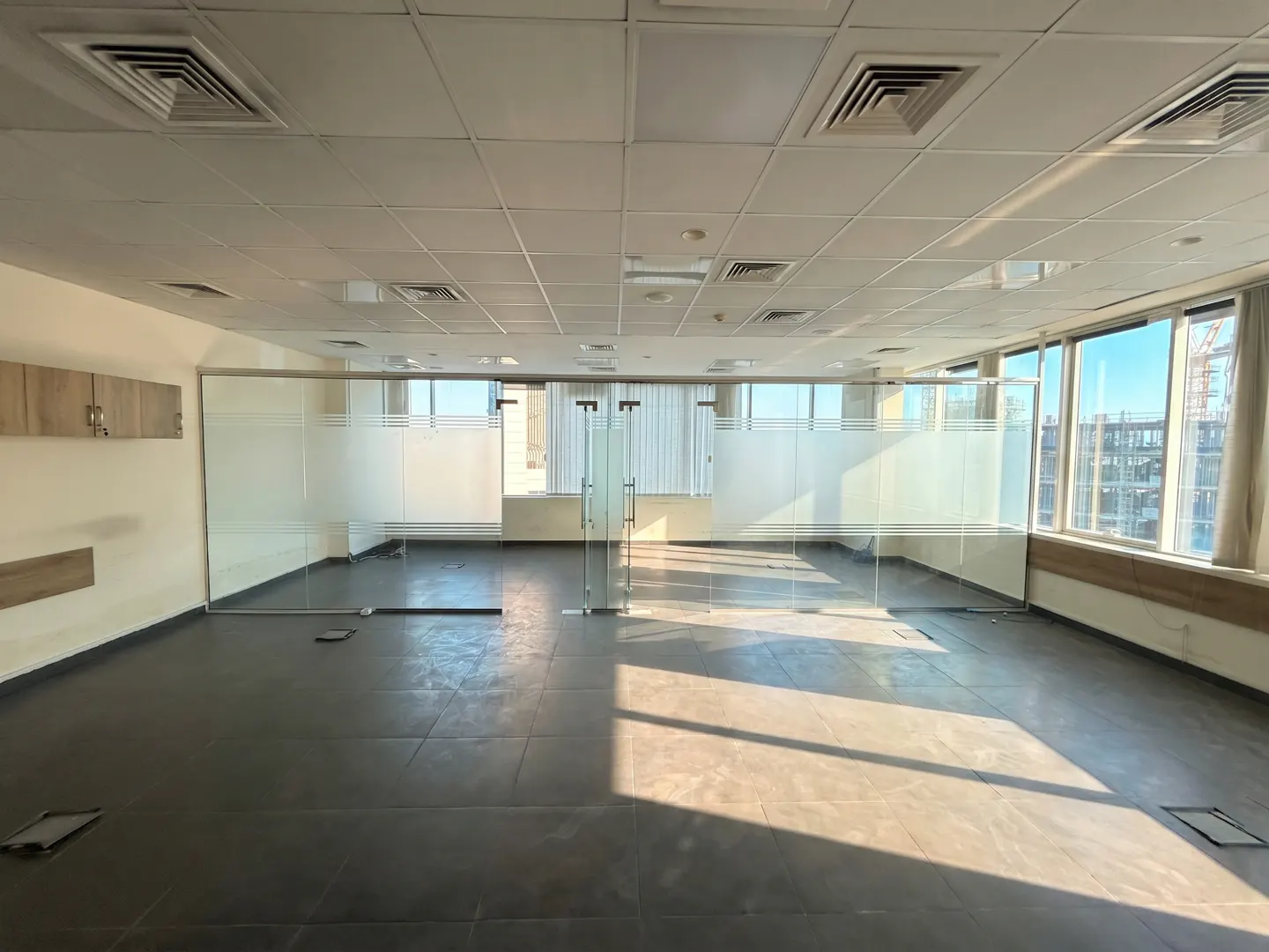 Empty office space with glass walls, dark tile floor, and large windows with a city view.