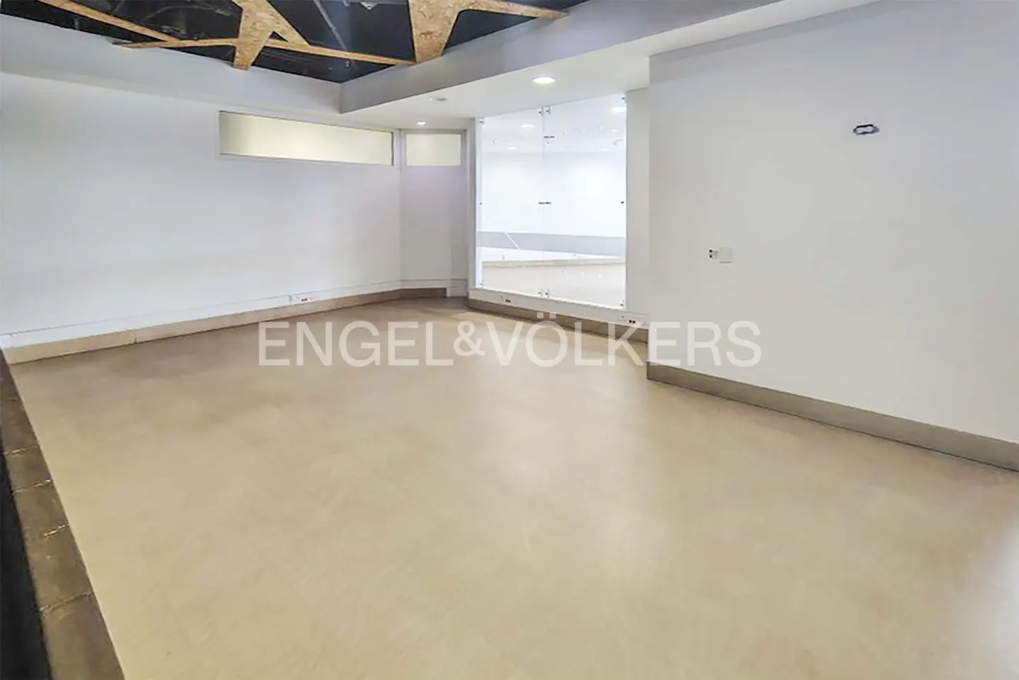 Empty room with beige floor, white walls, and glass partition. The ceiling has exposed wooden beams. Engel & Volkers logo is visible.