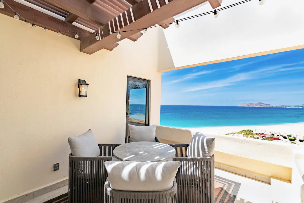Outdoor patio with a table and chairs overlooking a beach and ocean view.