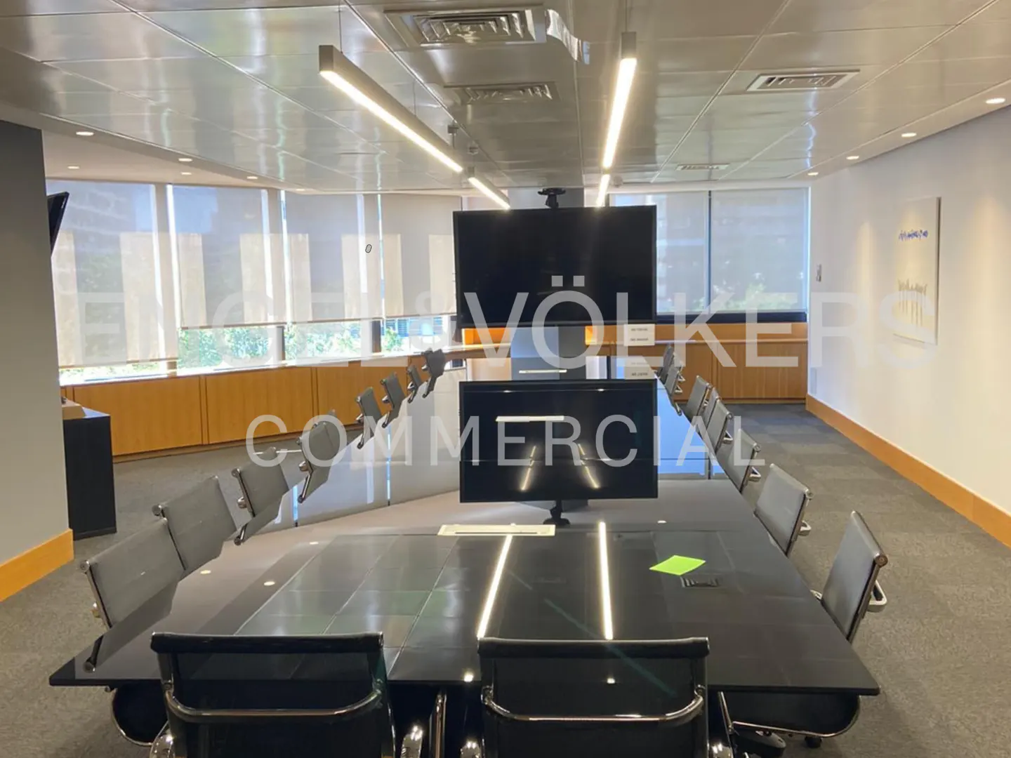 A modern conference room with a large black table, gray chairs, and two large screen monitors.