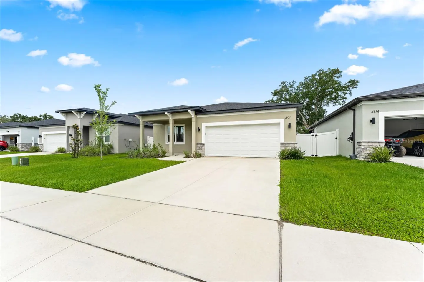 Modern single-story suburban home with a white garage, beige stucco exterior, and green lawn under a blue sky.