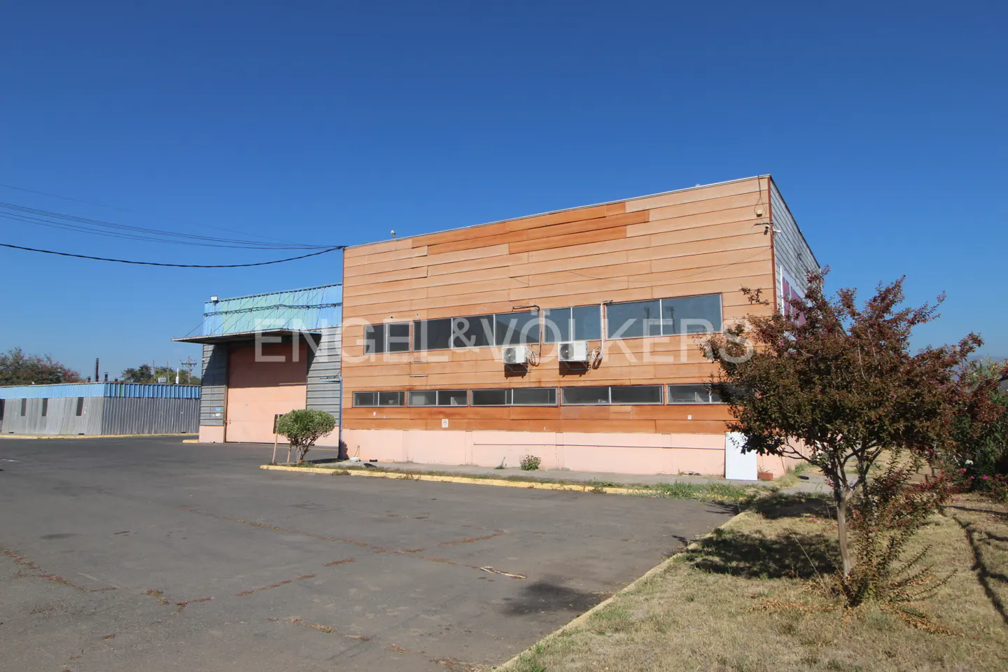 Exterior of a commercial building with wood paneling and a large parking lot under a clear blue sky.