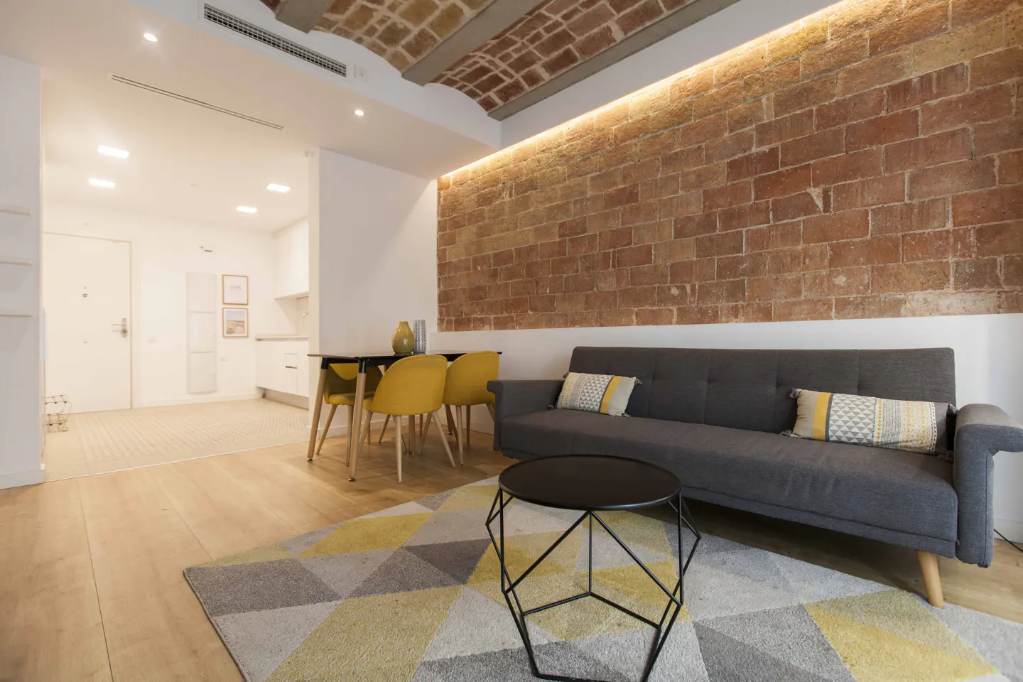Living room with exposed brick wall, gray sofa, yellow chairs, and geometric rug. Modern interior design.