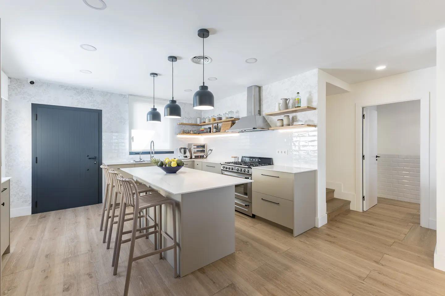 Modern kitchen with a white island, three pendant lights, light wood floors, and a dark grey door.