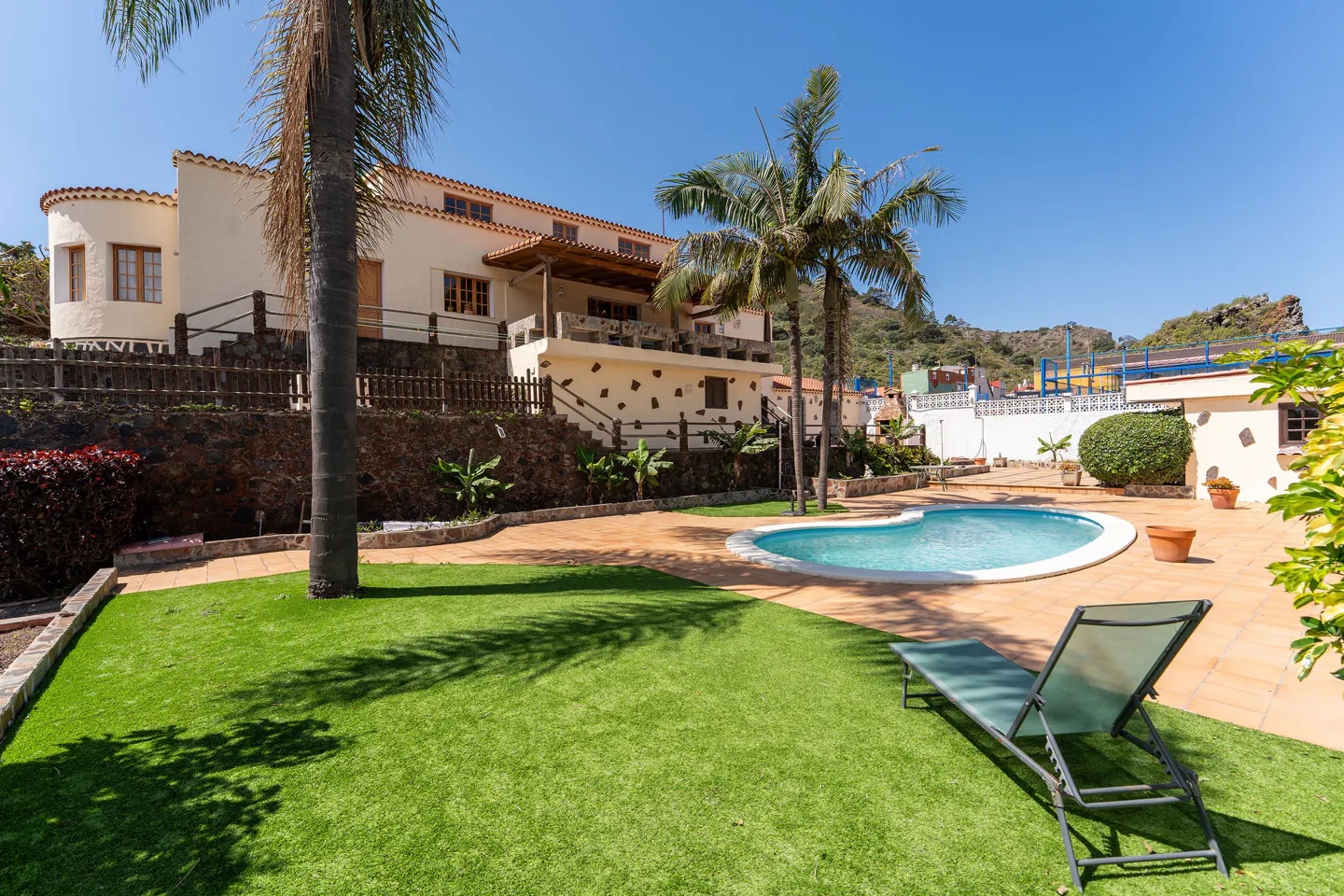 Exterior view of a cream-colored house with a pool, lawn, and lounge chair on a sunny day.