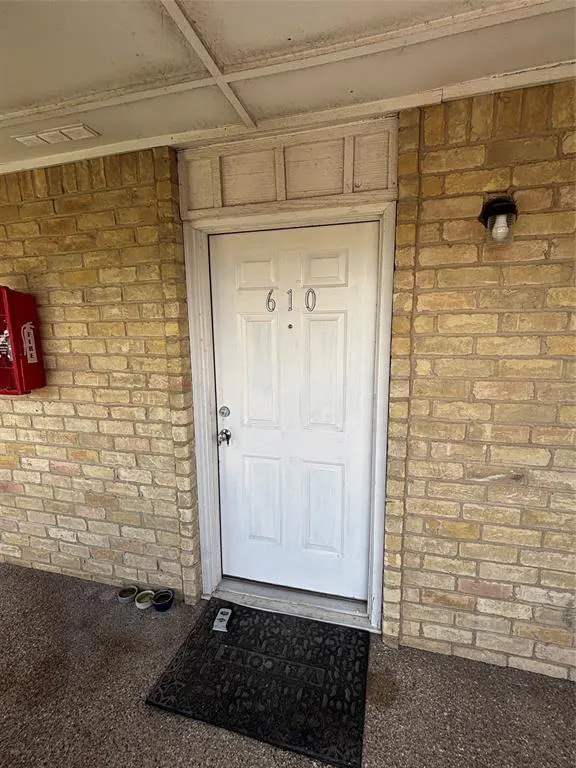 Exterior shot of a white door with the number 610 on a brick building. A black mat is in front of the door.
