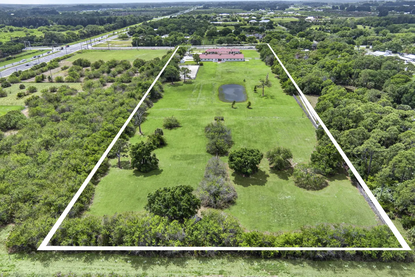 Aerial view of a large, green, rectangular property outlined in white, with a pond and a red-roofed building.