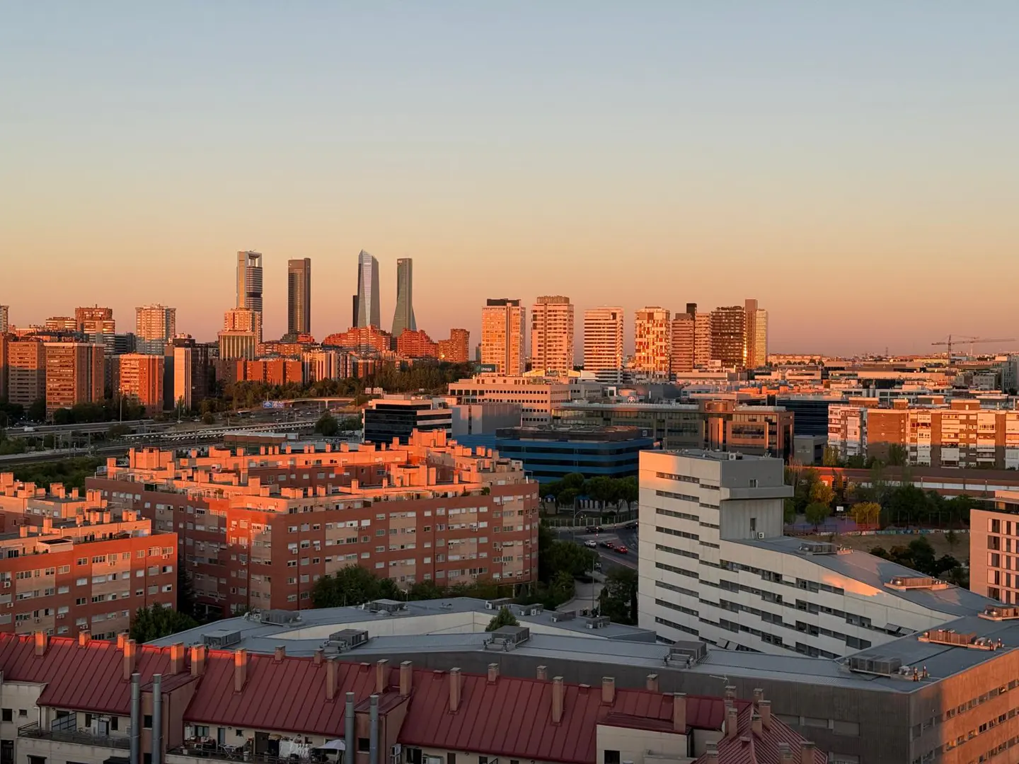 Cityscape view at sunset. Buildings are orange and red. Four skyscrapers are in the background.