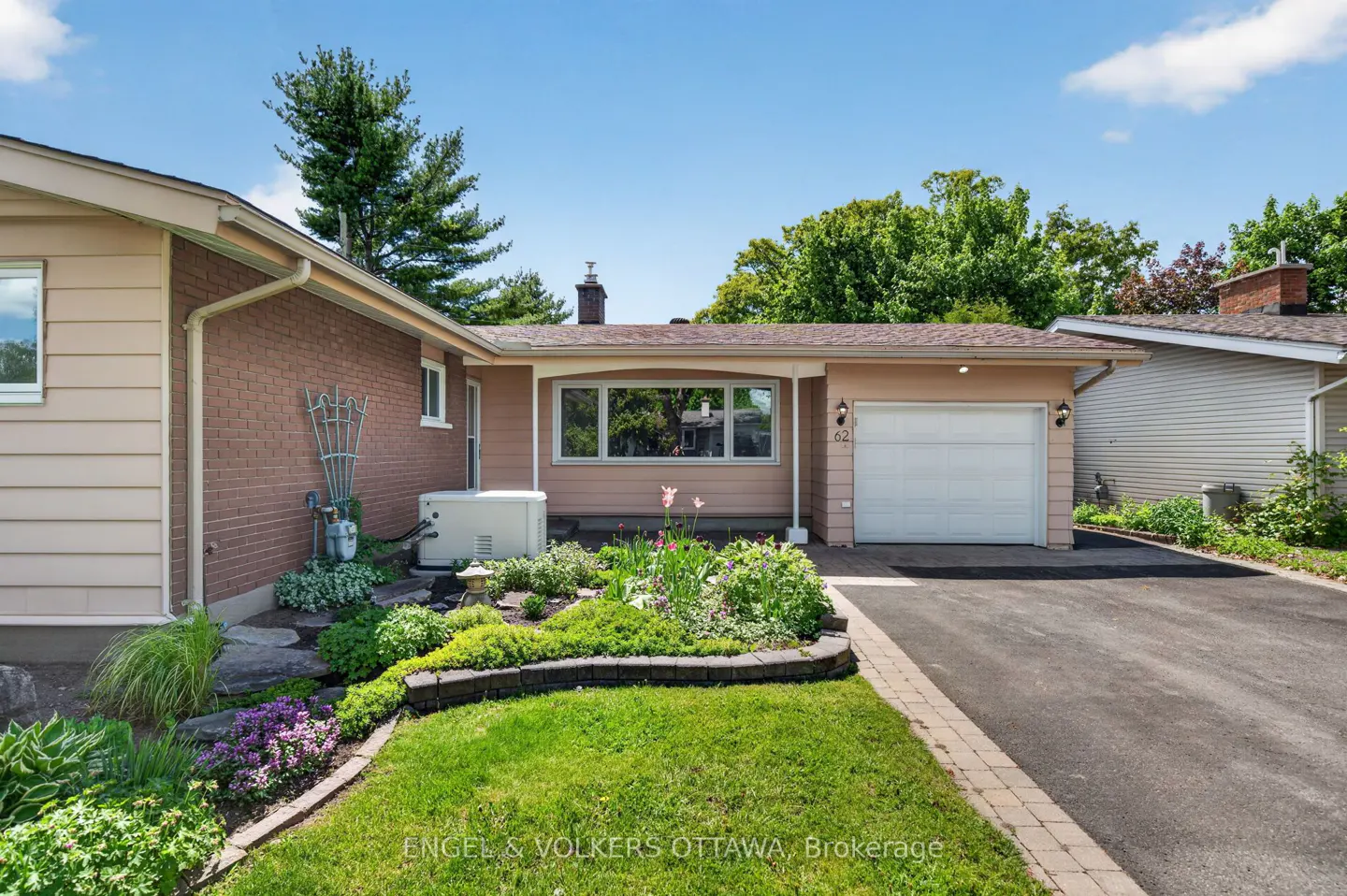 Exterior view of a single-story home with a tan facade, white garage door, and a well-manicured lawn and garden.