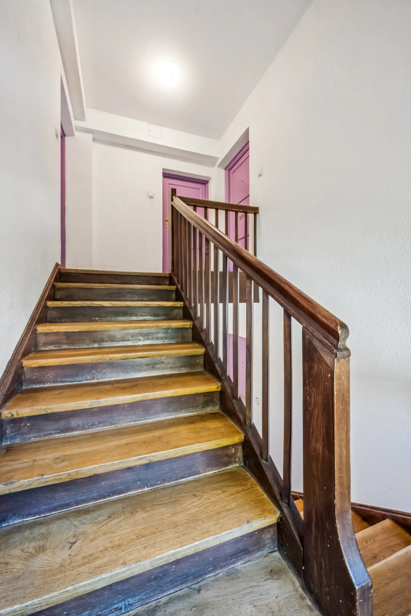 Wooden staircase with dark brown railing leads up to white walls and two purple doors.