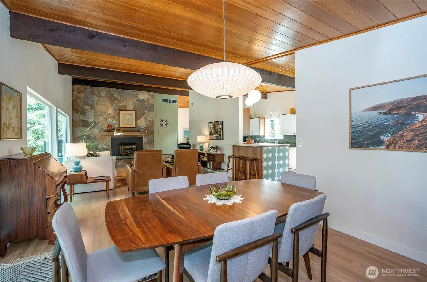 Open-concept living and dining area with wood ceiling, stone fireplace, and mid-century modern furniture.