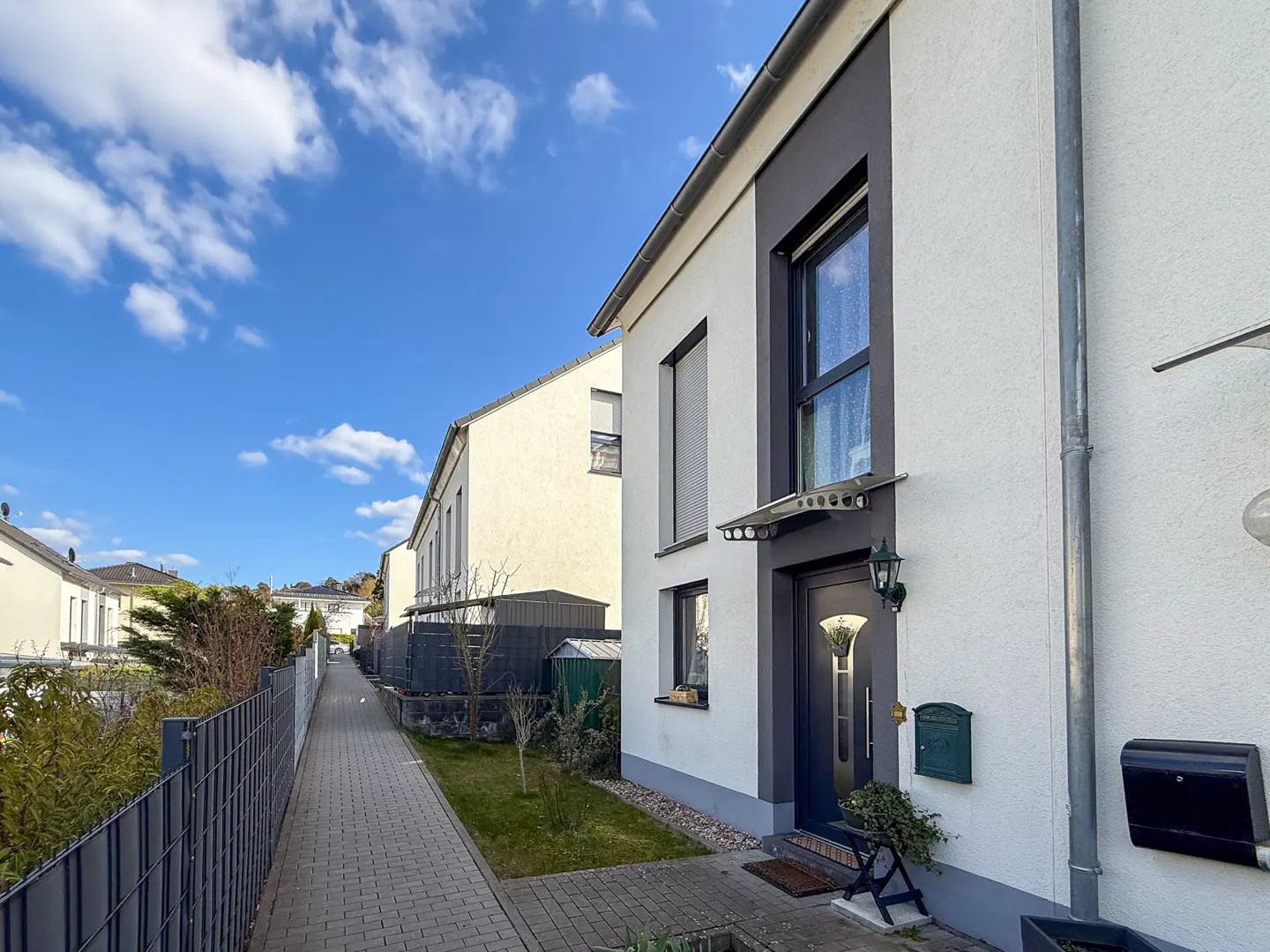 Exterior of a two-story white house with gray trim, a dark door, and a paved walkway under a blue sky.