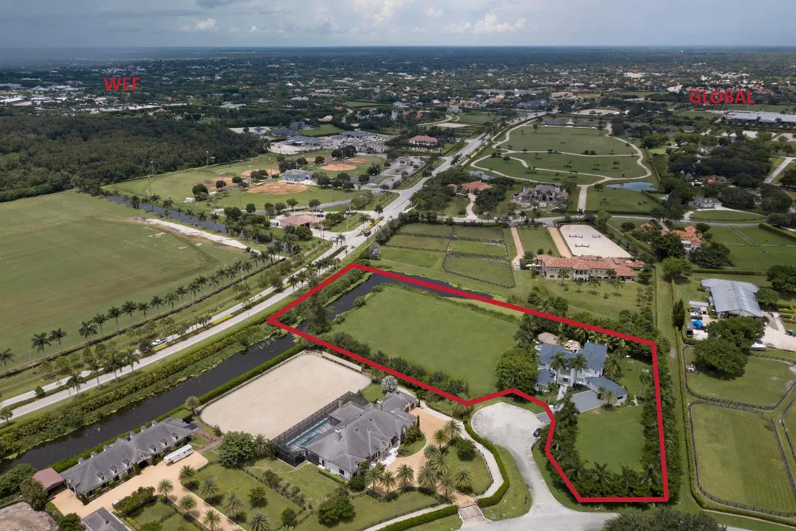 Aerial view of a property outlined in red, featuring a large green field, a white house, and surrounding greenery.