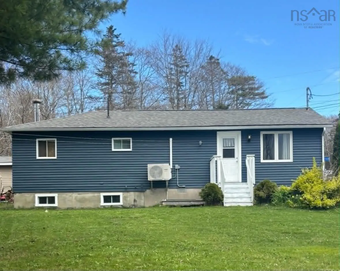 A one-story blue house with a gray roof and white trim sits on a green lawn under a blue sky.