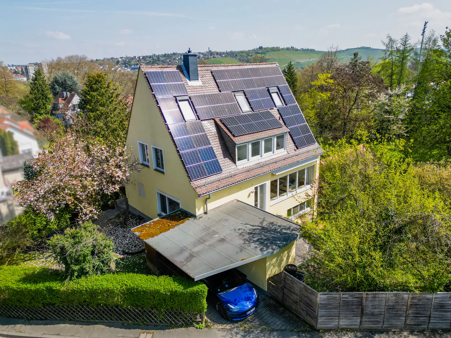 Two-story yellow house with solar panels on the roof and a blue car parked in the carport.