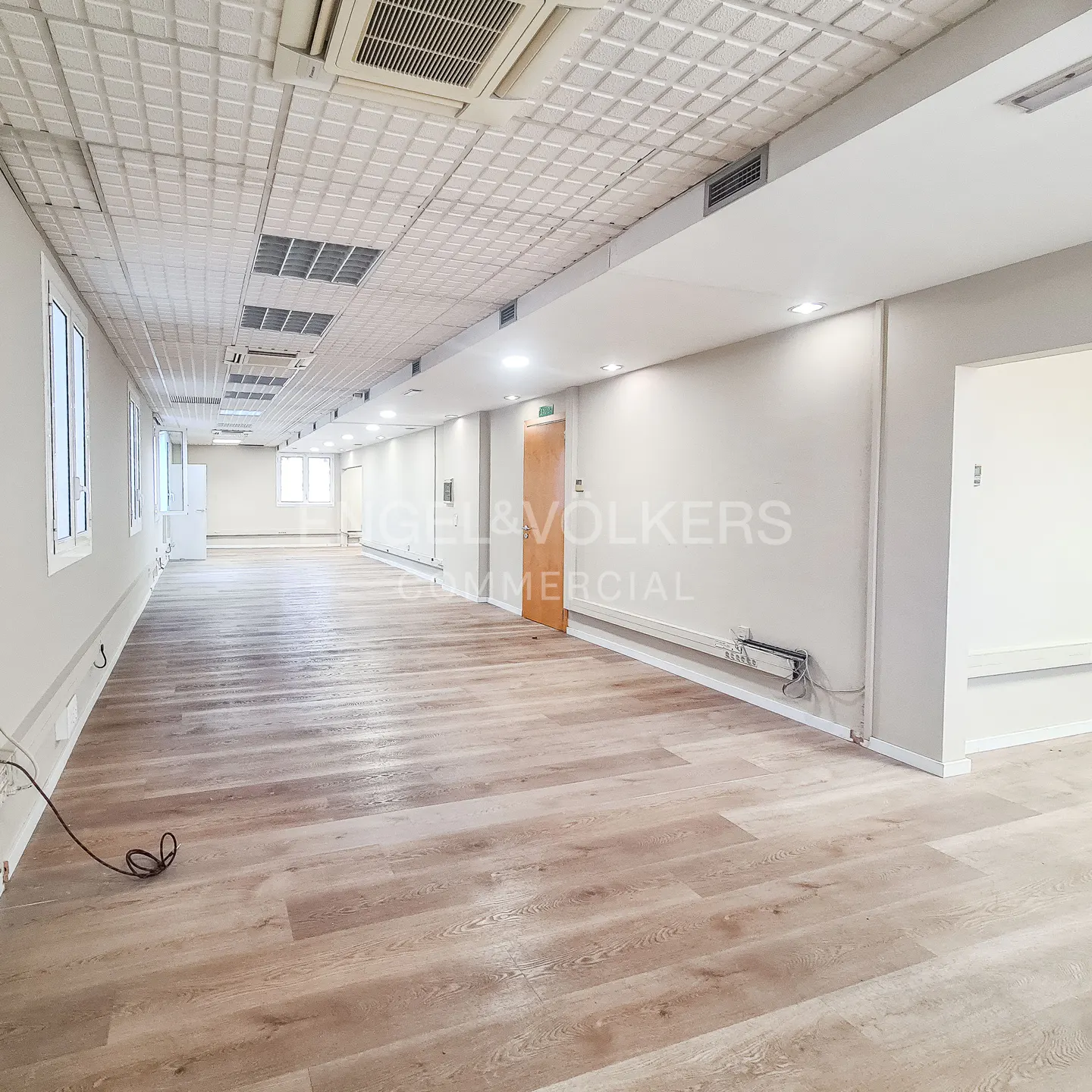 Bright, empty commercial space with light wood floors, white walls, and a textured white ceiling with vents and recessed lighting.