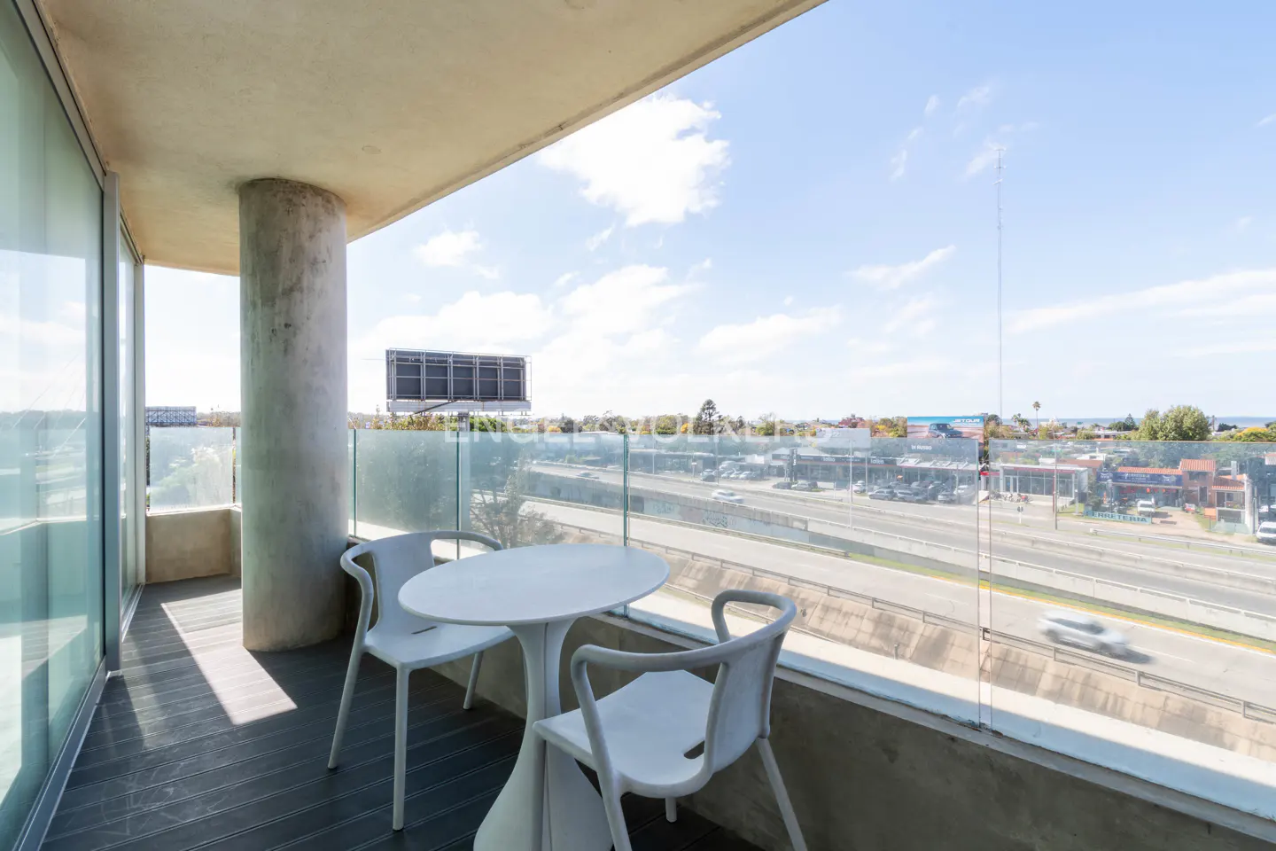 Balcony with a round white table and two chairs overlooking a highway and city skyline on a sunny day.