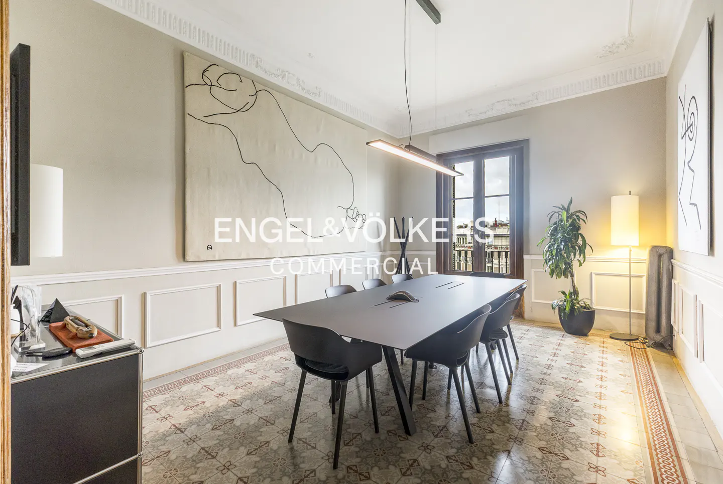 Modern conference room with a long black table, black chairs, patterned tile floors, and large abstract line art on walls.