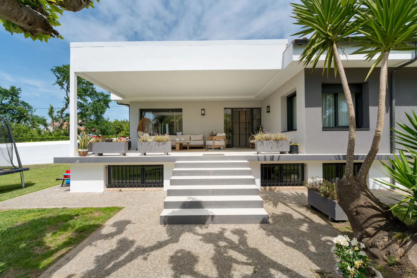 Exterior view of a modern two-story house with a white porch, gray stairs, and green lawn.