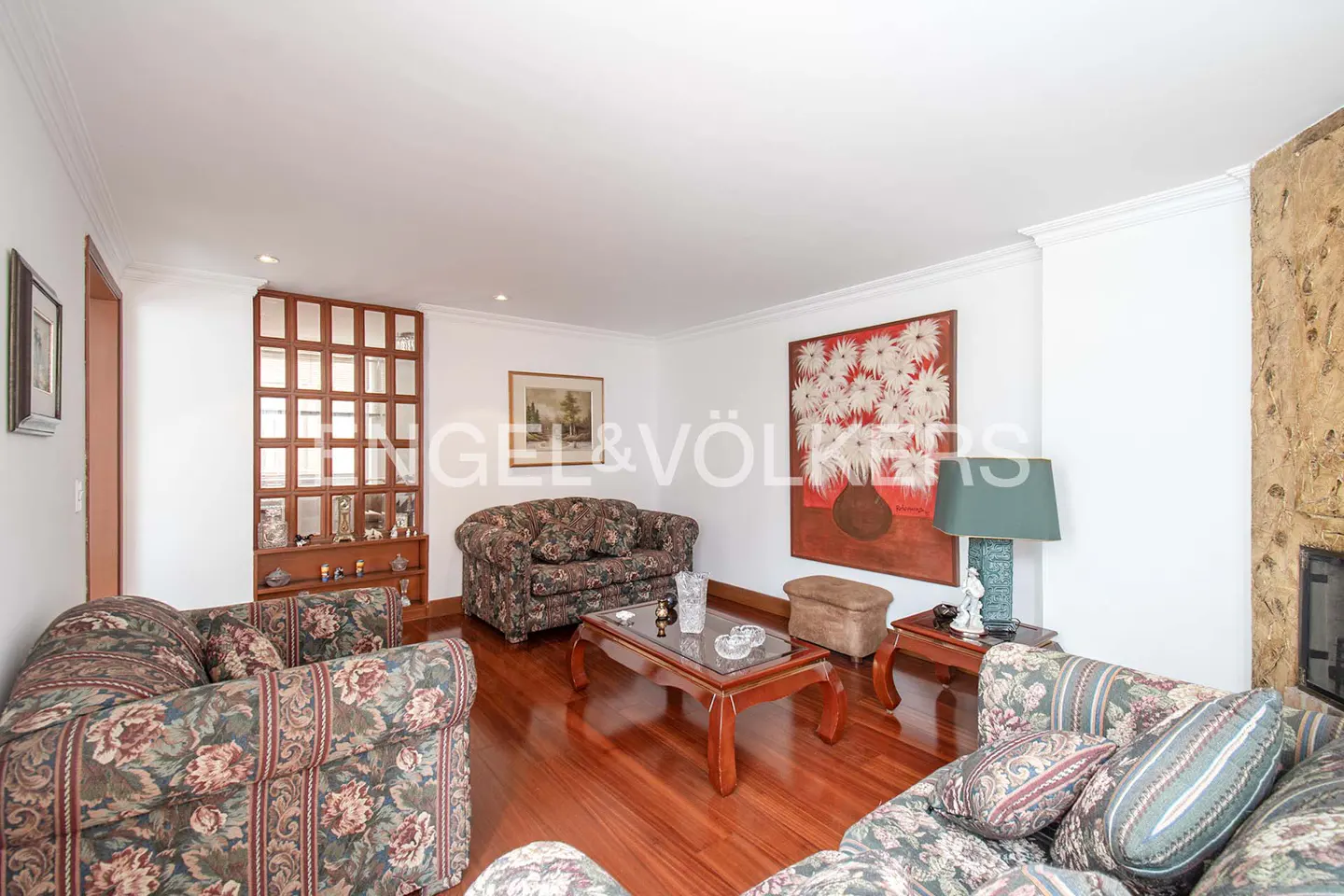 Living room with floral sofas, wooden coffee table, large floral wall art, and a stone fireplace feature on hardwood floors.