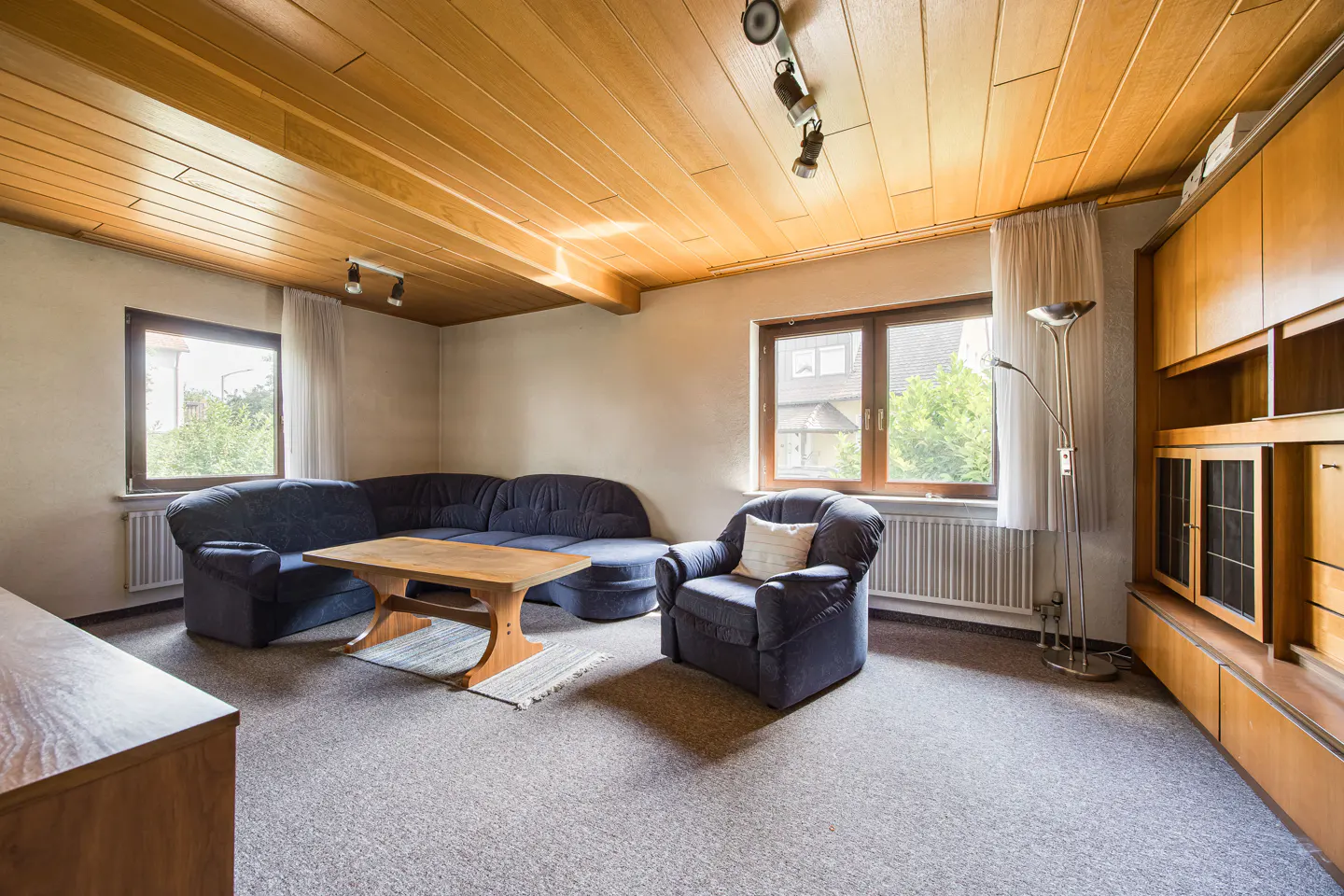 Living room with wood-paneled ceiling, blue sofa and armchair, wood table, and built-in wood cabinets.