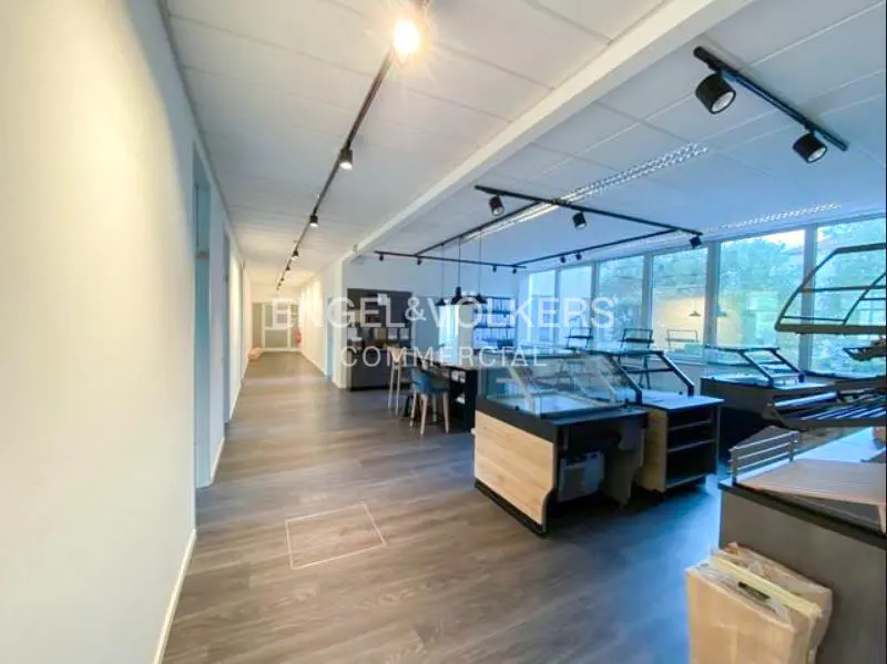 Bright commercial space with wood floors, display cases, and Engel & Volkers signage. Track lighting illuminates the area.