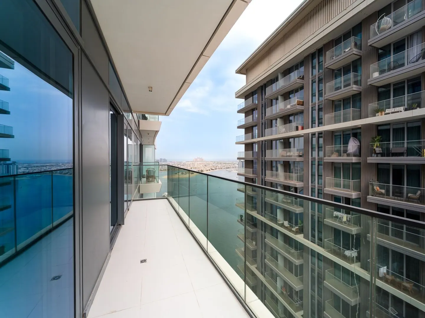 View from a high-rise balcony with glass railings, overlooking water and city skyline. Another building is visible to the right.
