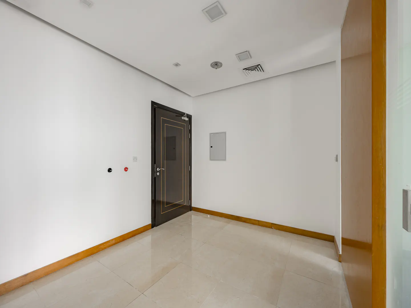 Empty room with white walls, beige tile floor, and a dark brown door with gold trim.